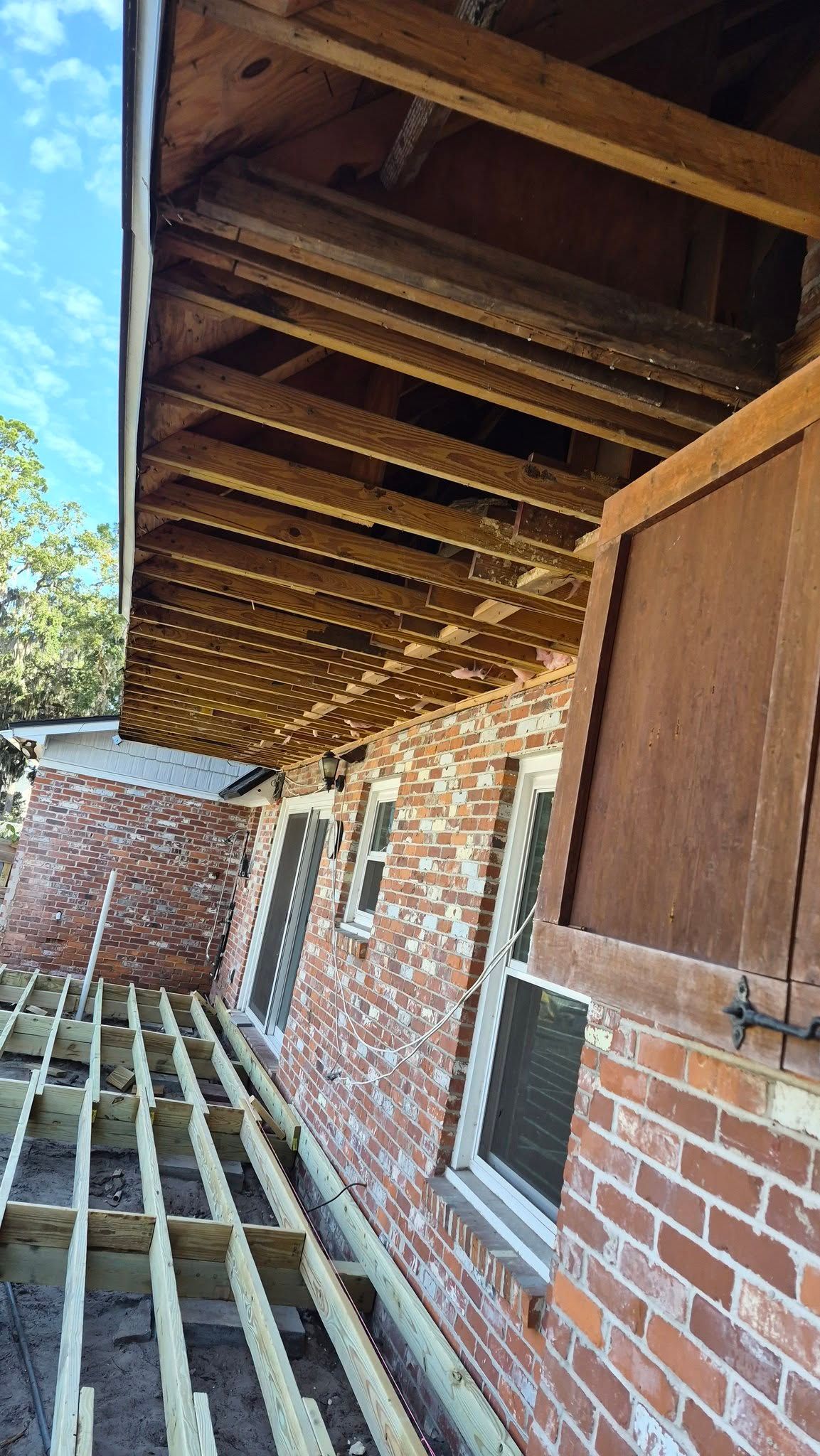 Brick house exterior with wooden overhang and scaffolding along the side wall