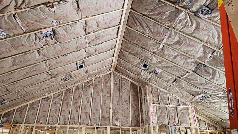 Interior of a building under construction with exposed roof trusses and insulation in the ceiling