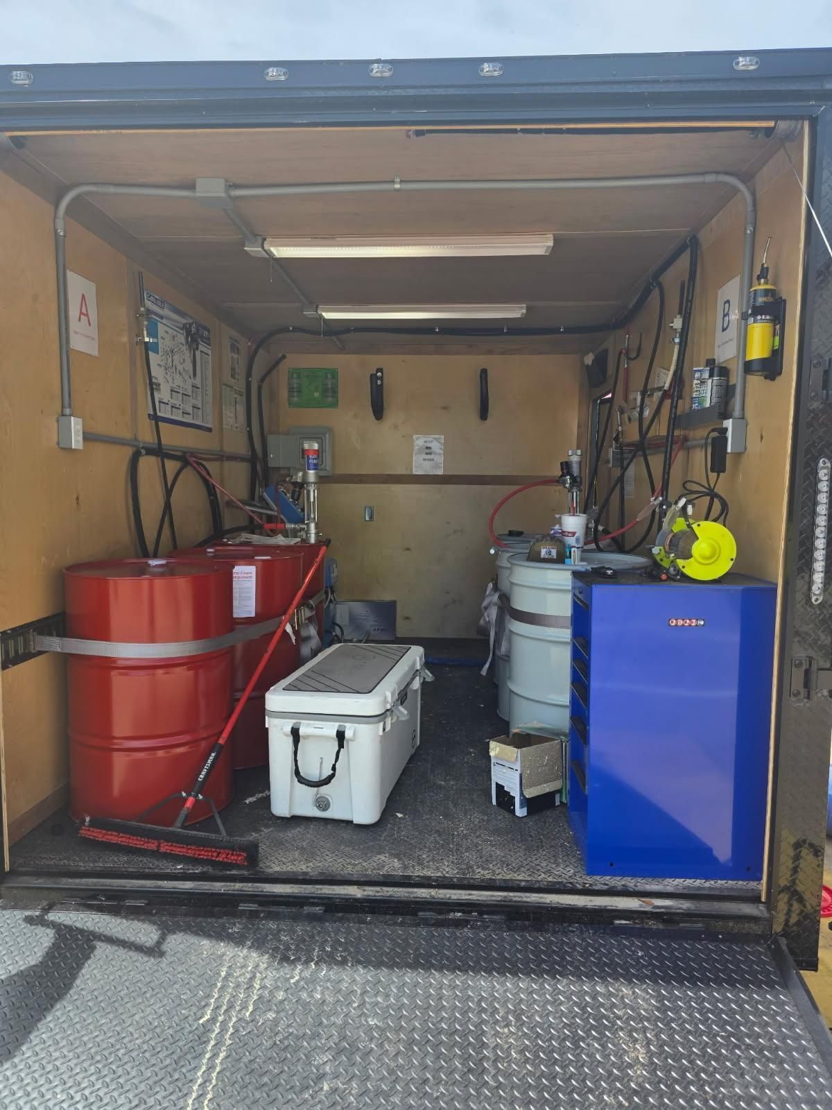 Storage trailer with barrels, cooler, and blue cabinet inside an open cargo space