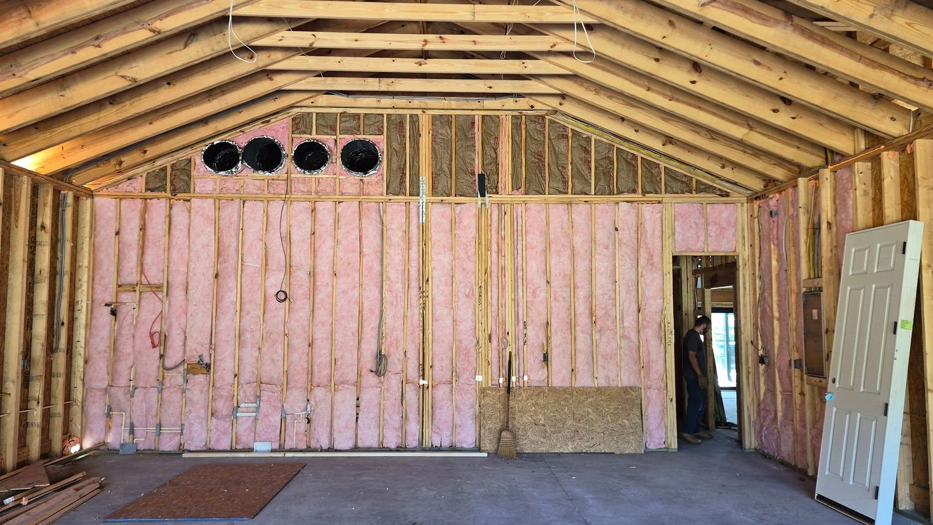 Unfinished wooden interior with pink insulation, exposed rafters, and a doorway on the right.