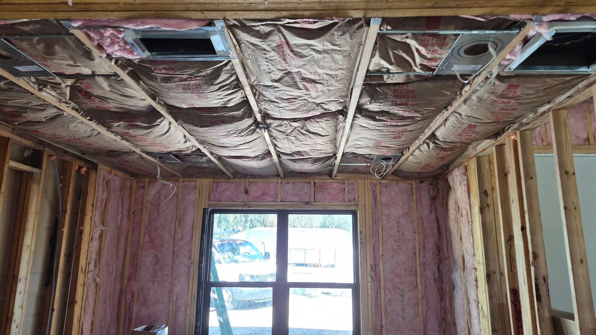 Exposed ceiling insulation and framing in an unfinished room with a window at the far end.