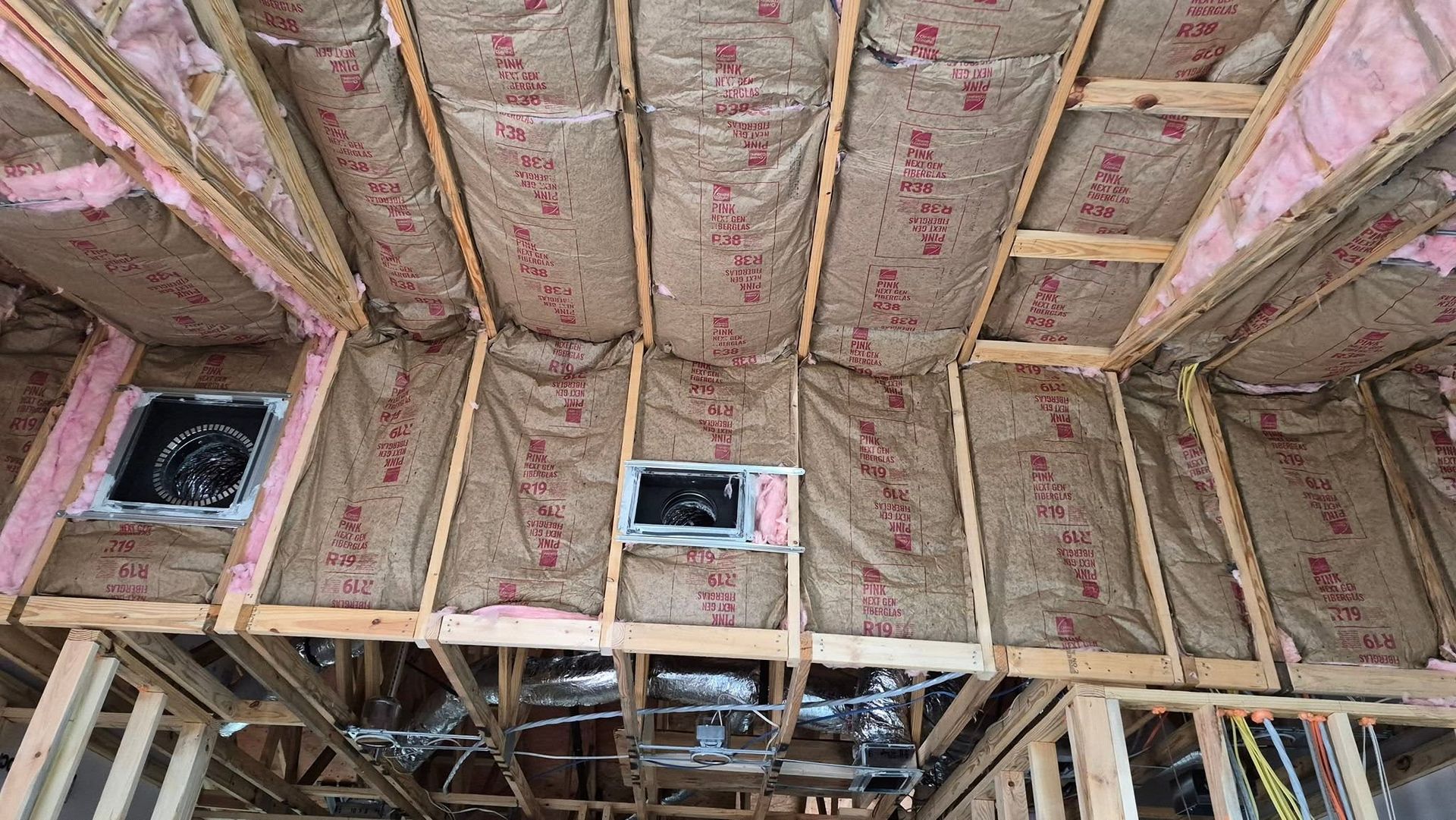 Insulated ceiling framing with pink fiberglass batts and three recessed light openings in a room under construction