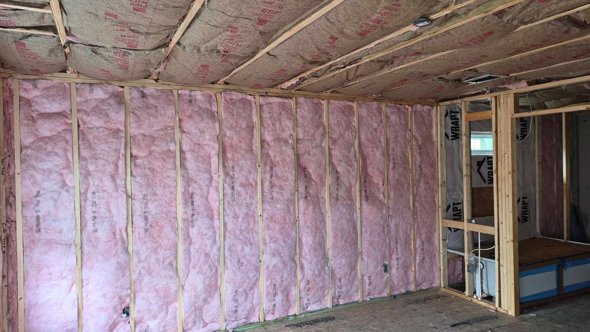 Unfinished room with pink fiberglass insulation in walls and ceiling framing exposed.