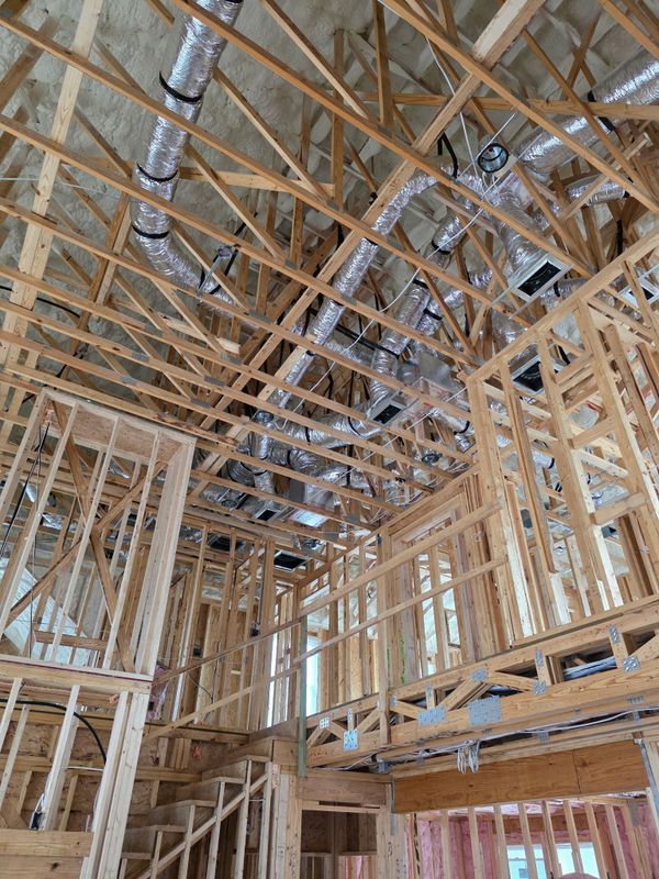 Interior of a house under construction, showing exposed wooden framing and ductwork on the ceiling.