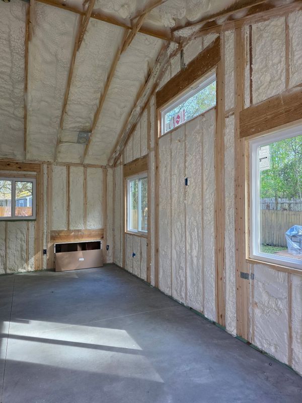 Unfinished insulated room with exposed framing, windows, and a small fireplace opening.