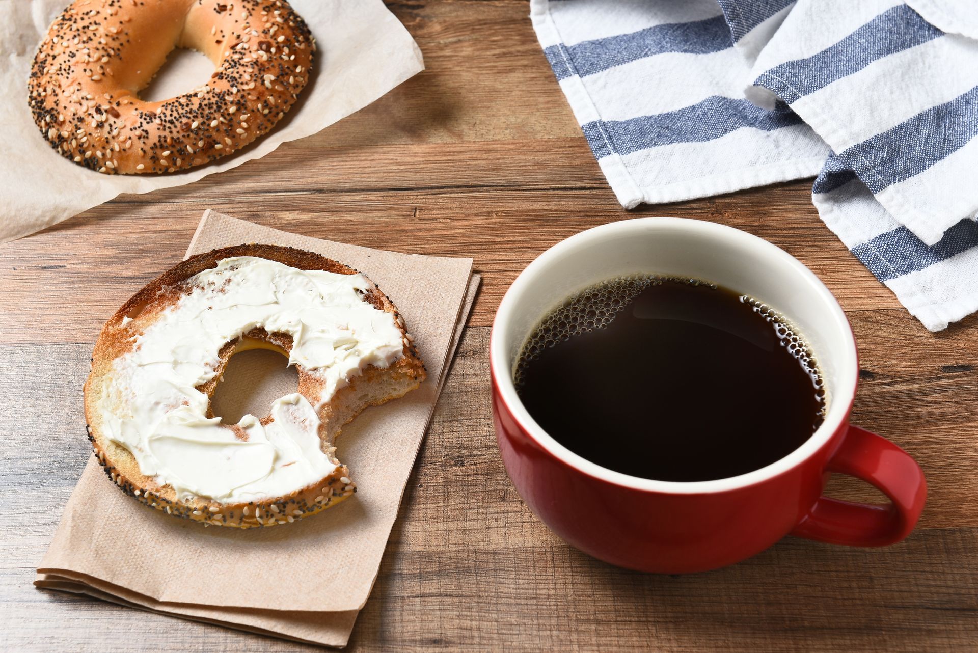 A bagel with a bite taken out of it and a cup of coffee on a wooden table.