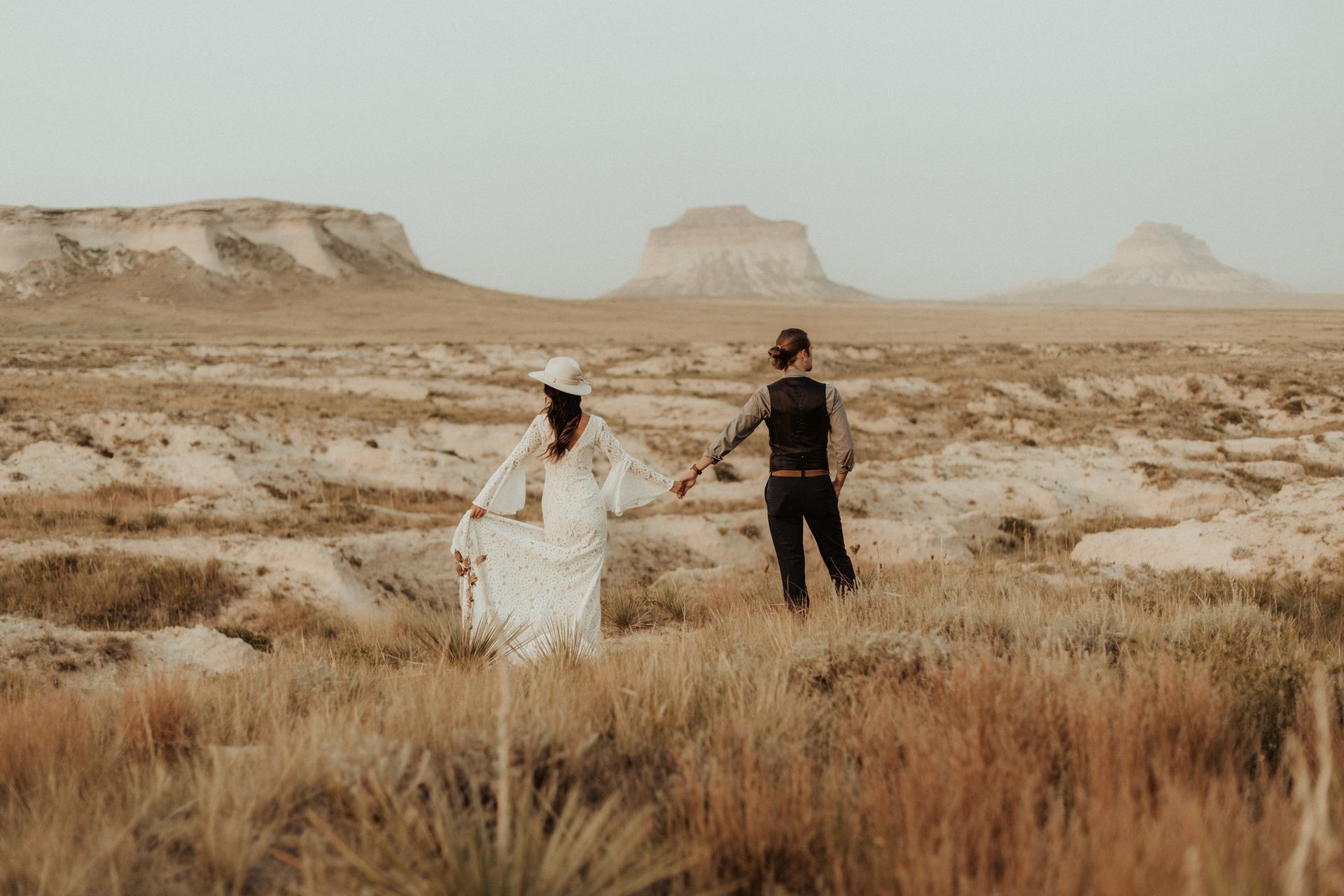 A bride and groom are walking through a desert holding hands.