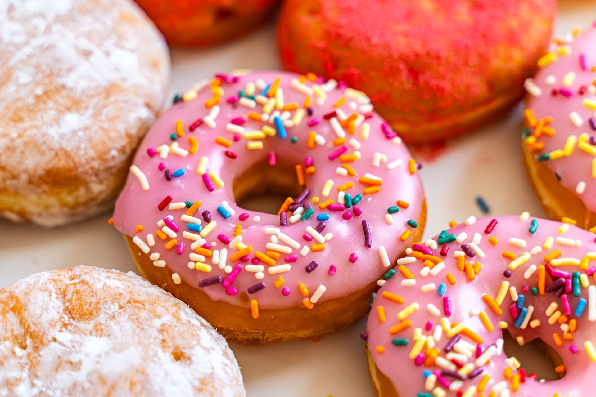 A close up of a plate of donuts with pink frosting and sprinkles.