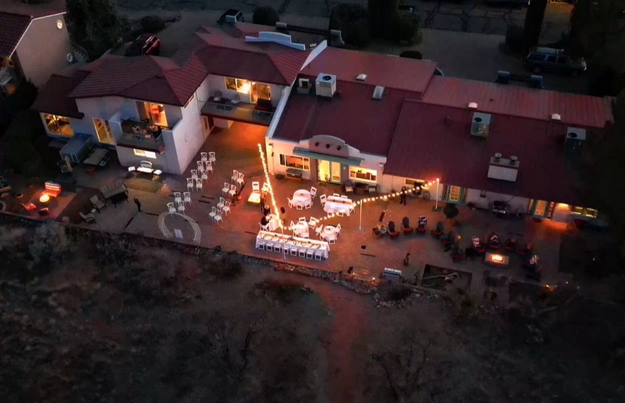 An aerial view of a large house with tables and chairs outside at night.
