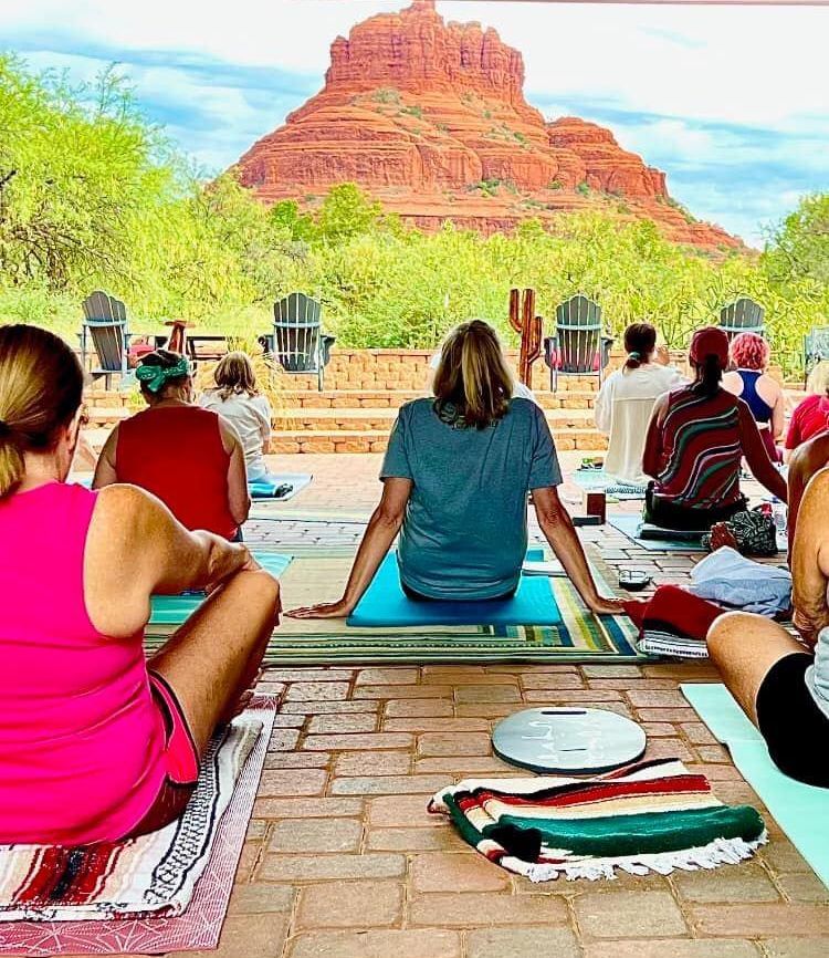 A group of people are sitting on yoga mats in front of a mountain.