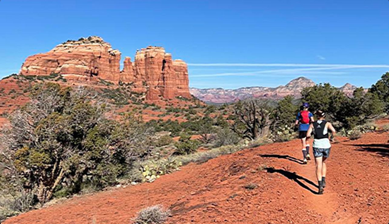 Two people are walking down a dirt path in the desert.