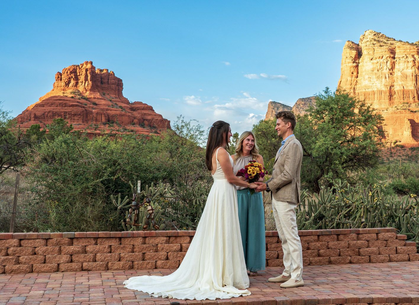 A bride and groom are holding hands during their wedding ceremony in front of a mountain.