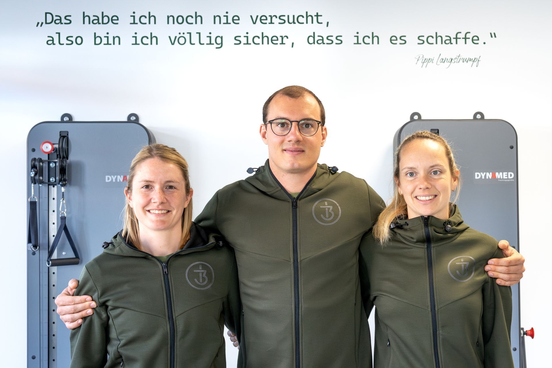 Ein Mann und zwei Frauen posieren für ein Foto vor einer Wand mit einem Zitat darauf.