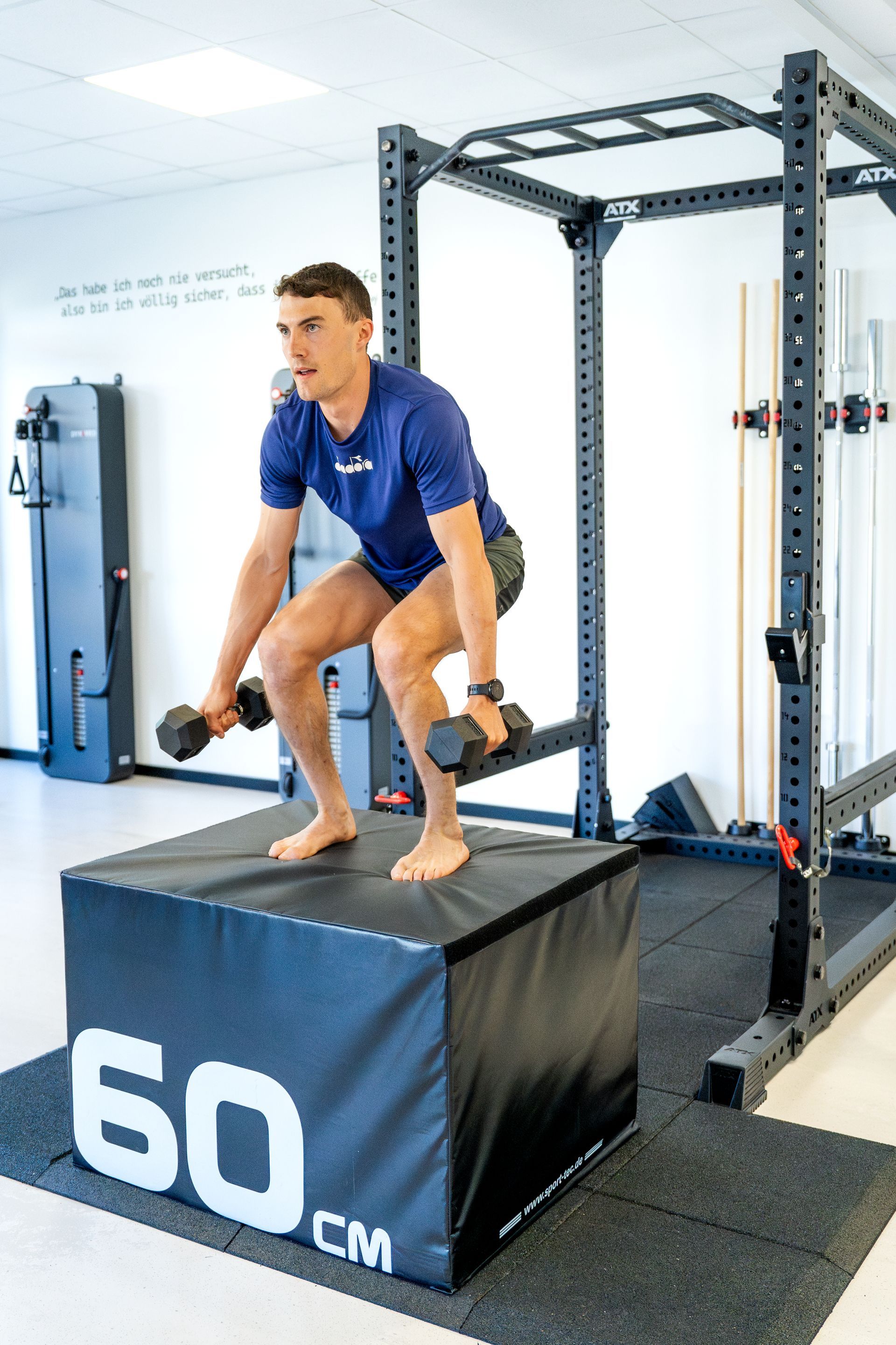 Ein Mann springt in einem Fitnessstudio mit Hanteln auf einer Box.