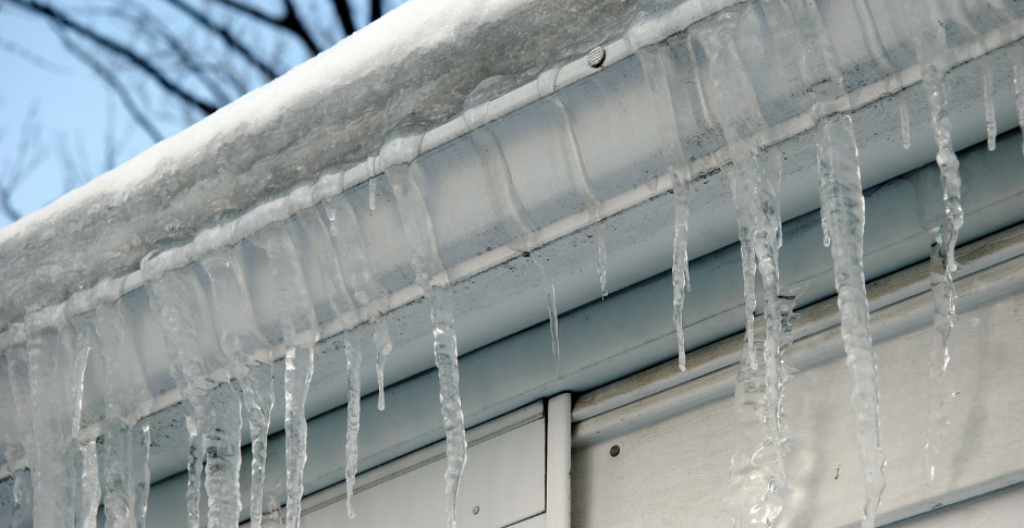 Icicles hanging from a snow-covered roof edge against a blue sky