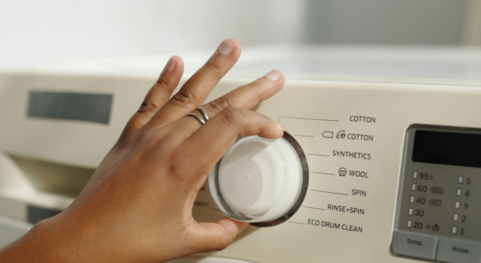 A hand turning the dial of a beige washing machine to select a laundry cycle.