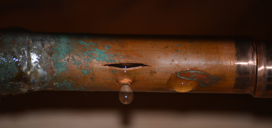 Rusty copper pipe with a corroded hole leaking water drops