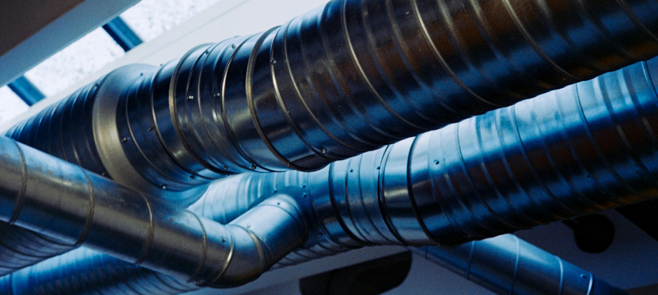 Blue industrial air ducts and ventilation pipes crossing a ceiling.