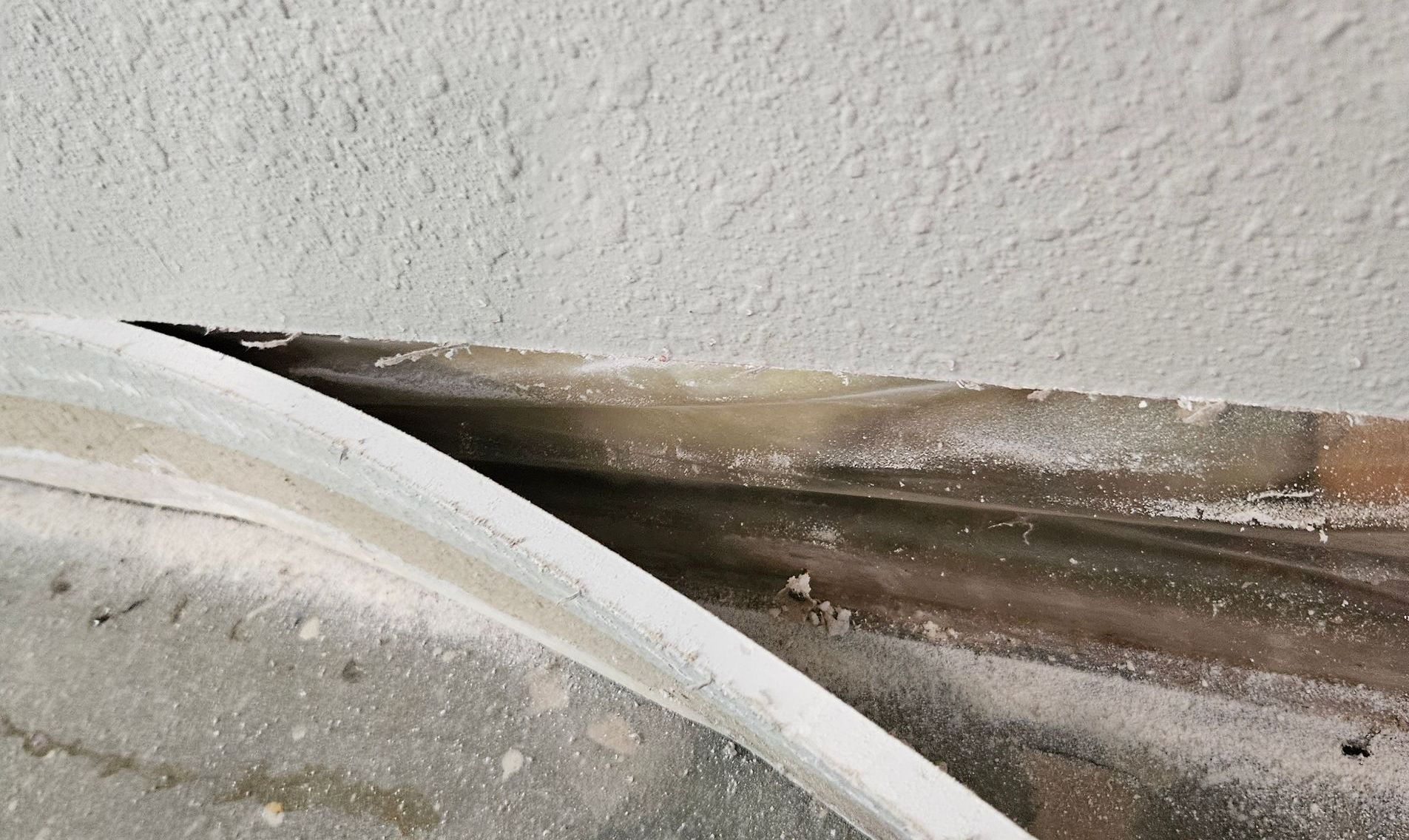 A close-up of white curved trim and a brown ledge with dirt and peeling paint near a wall.