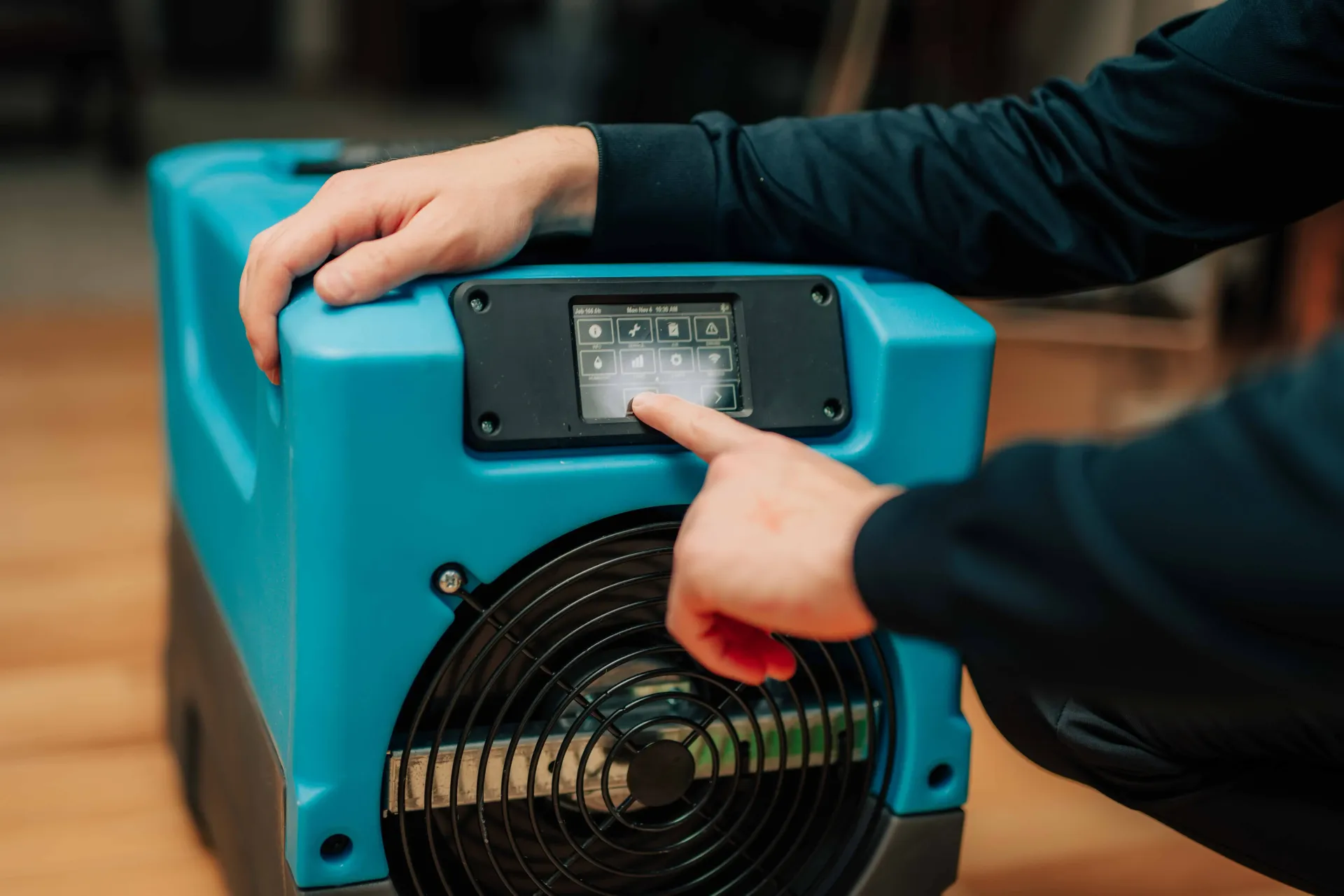 A person is pressing a button on a blue dehumidifer.