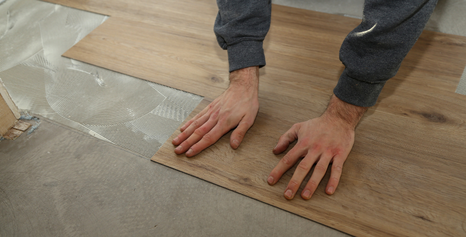 Hands aligning wood-look flooring tiles beside a carpeted area during installation