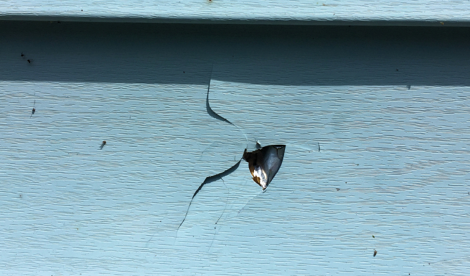 Cracked and damaged light blue siding with a triangular hole and exposed material.