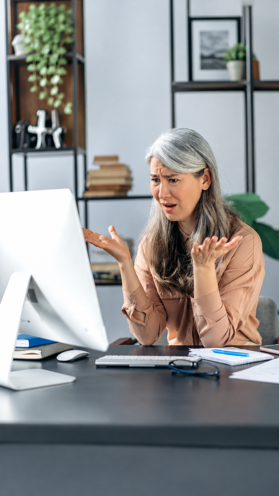Woman gesturing beside a desktop computer in a modern office, looking surprised