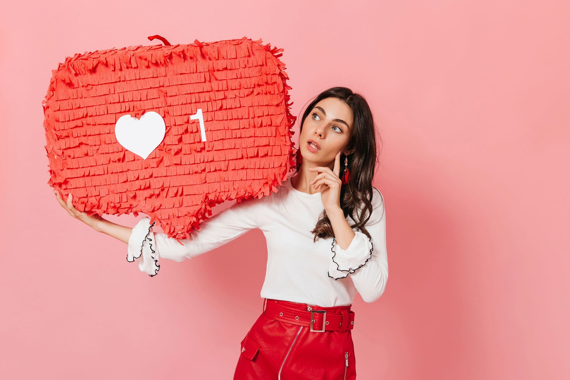A woman is holding a piñata in the shape of a heart.