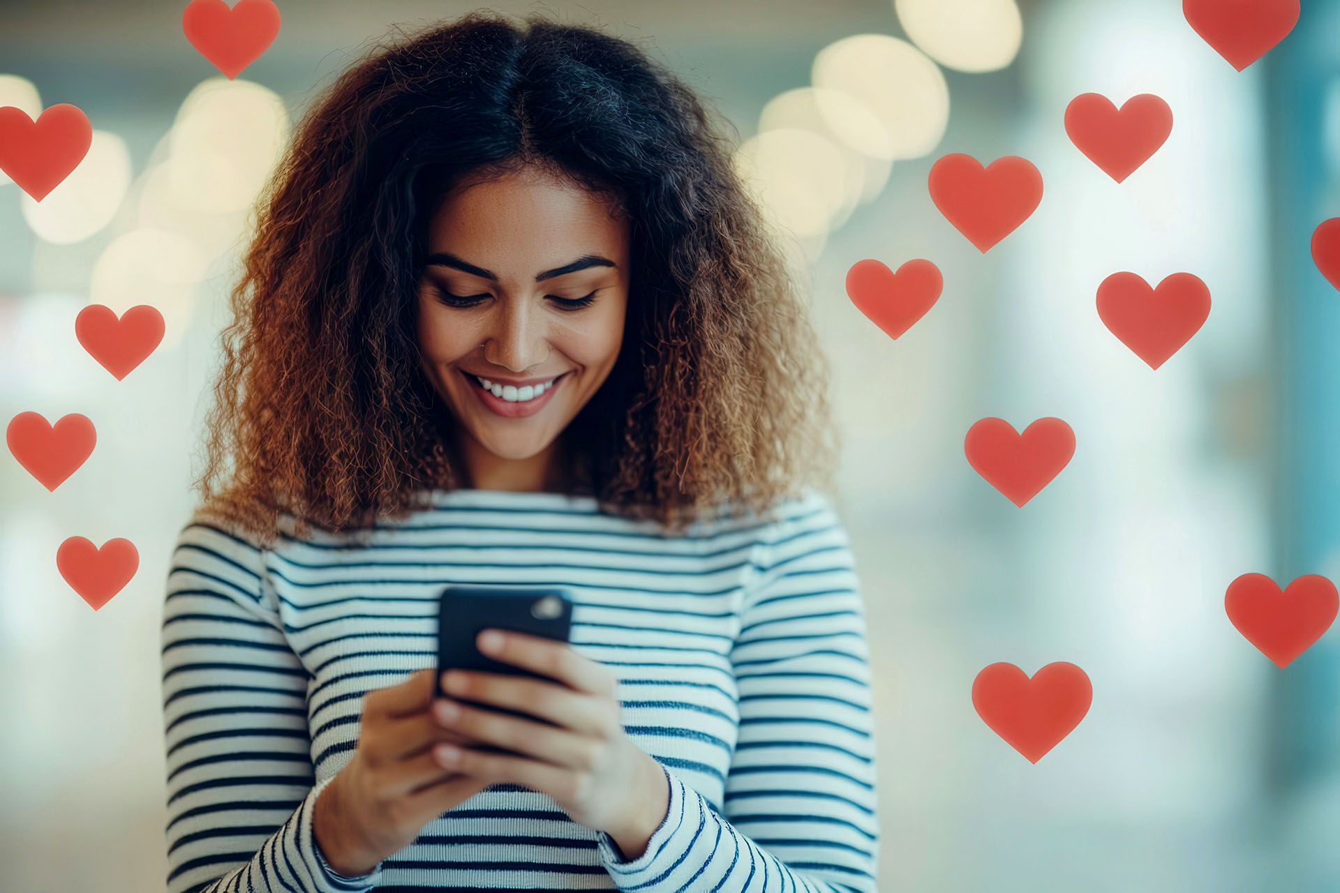 A woman is smiling while looking at her cell phone with hearts flying around her.