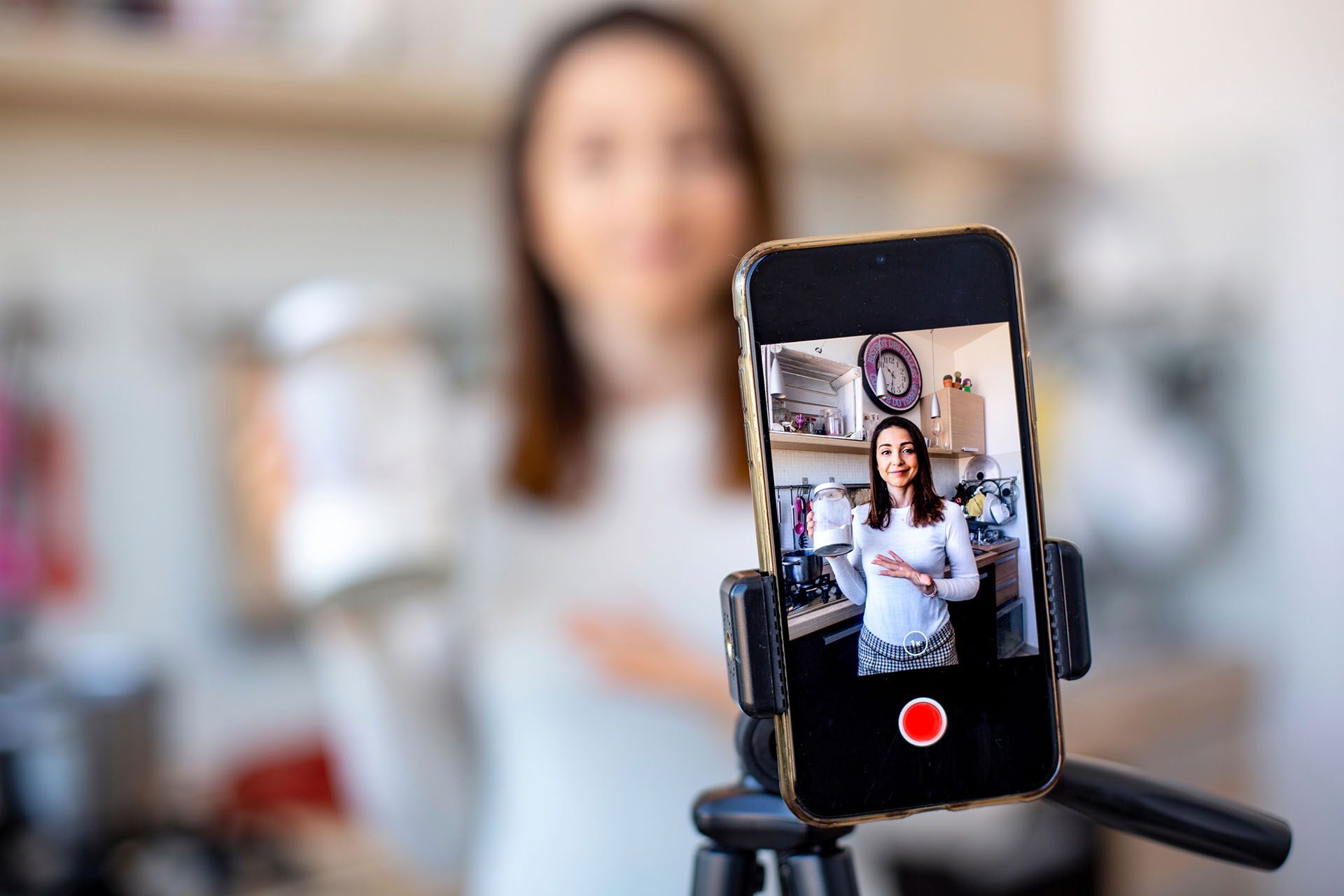 A woman is recording a video on a cell phone on a tripod.