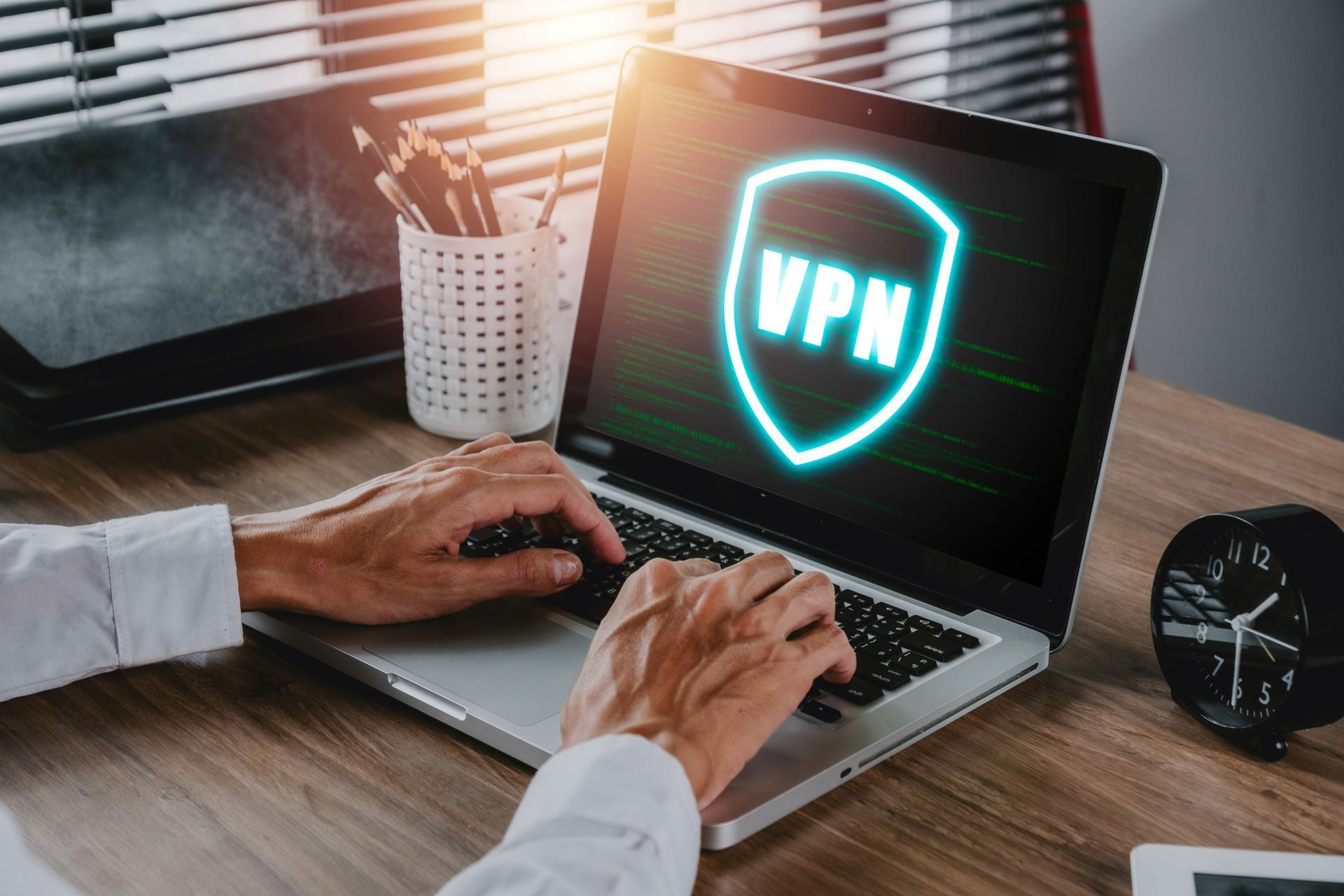 Person typing on a laptop displaying a VPN logo, with a desk setting.