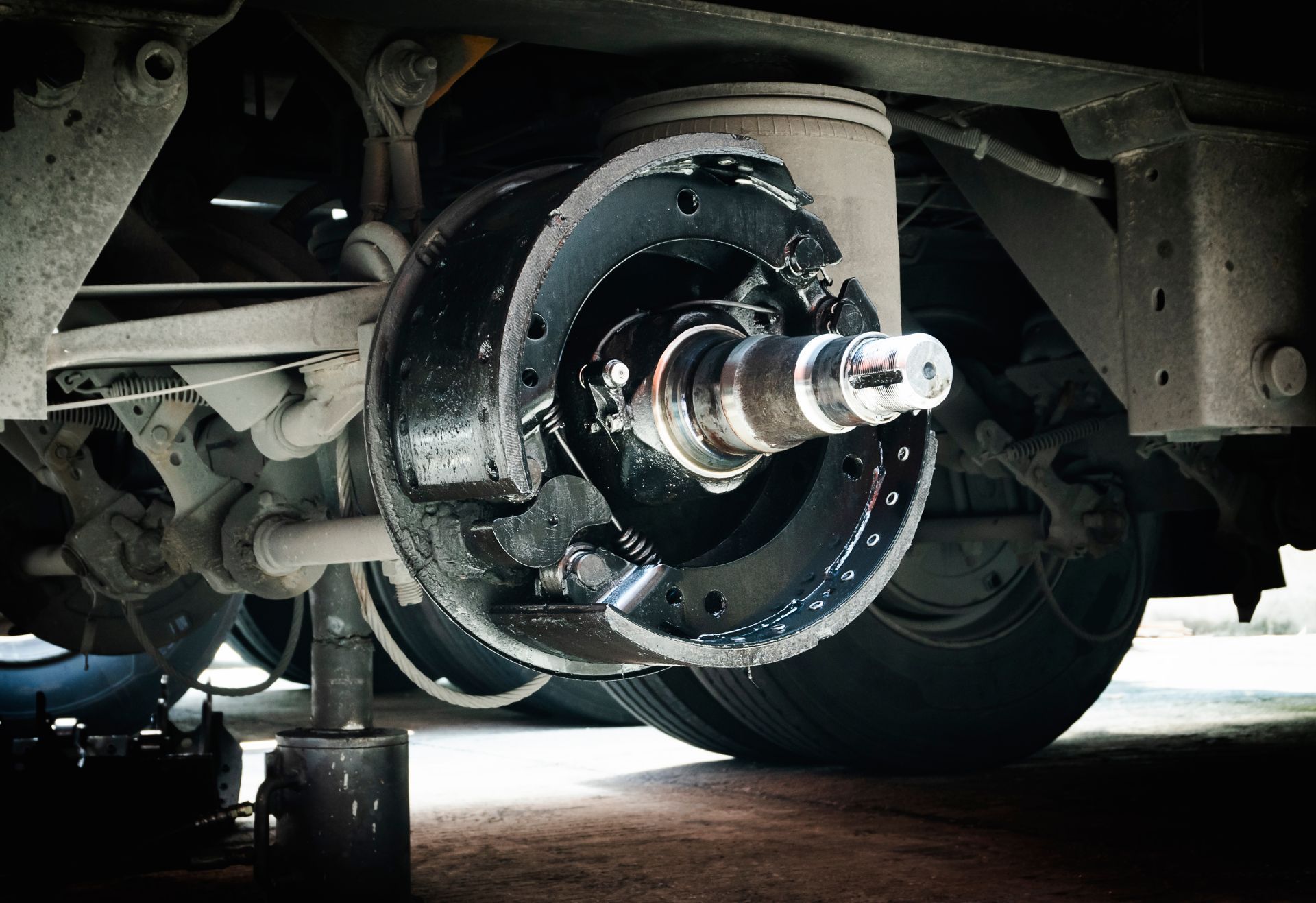 A close-up of a heavy-duty truck's exposed wheel assembly with visible brake shoes, spindle, and suspension parts.