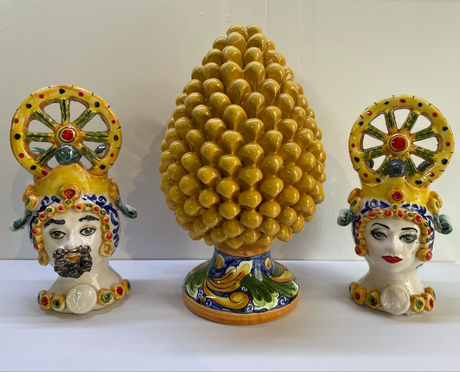 Teste siciliane in ceramica con ruote e un oggetto a forma di pigna nei colori giallo, blu e verde.