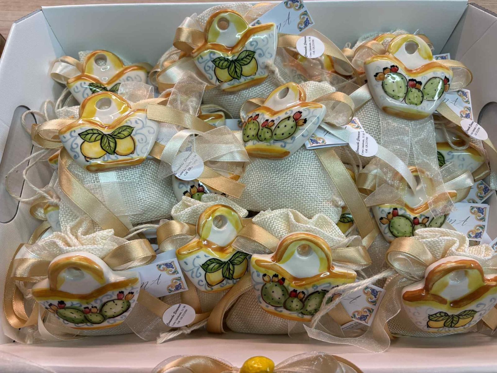 Ornamenti in ceramica a forma di limone su sacchetti di tessuto color avorio, legati con un nastro, in un vassoio bianco.