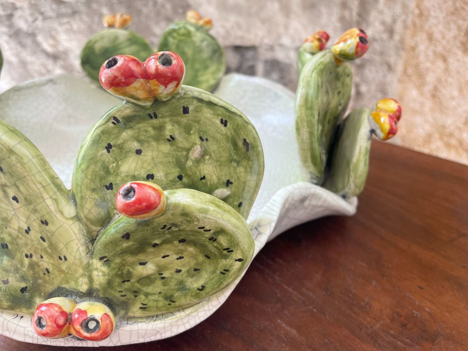 Ciotola di cactus in ceramica con foglie verdi, frutti rossi e bordo bianco su una superficie di legno.