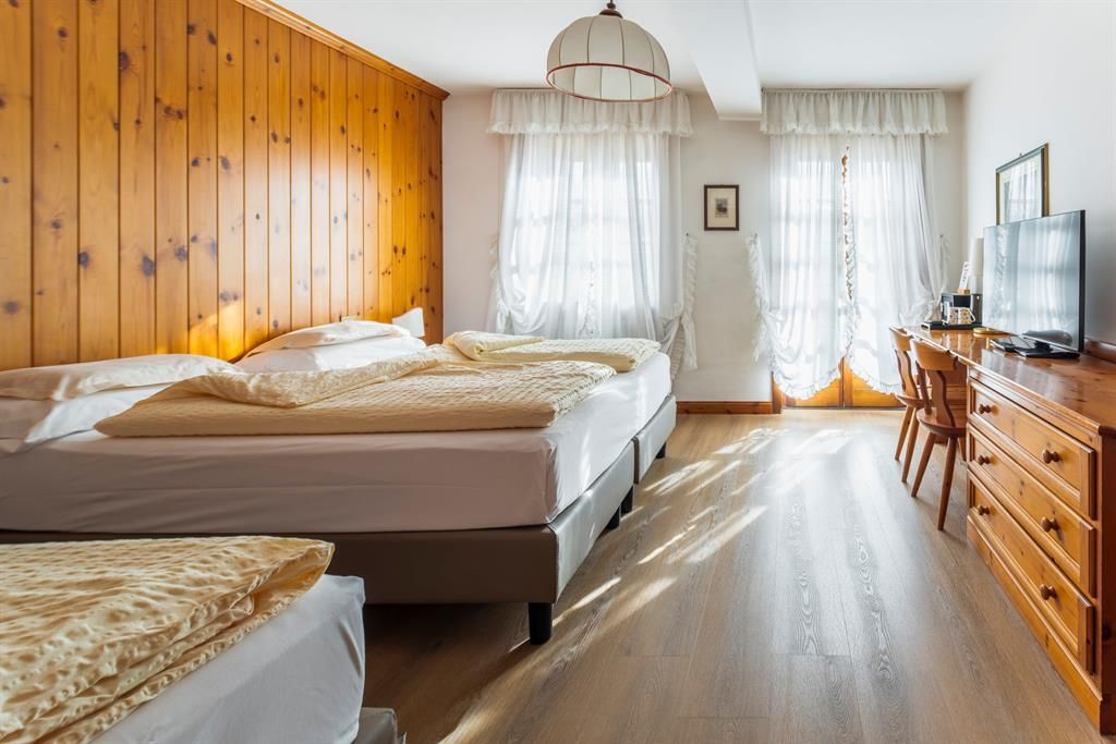 Ein Hotelzimmer mit drei Betten, einer Kommode und einem Fernseher.