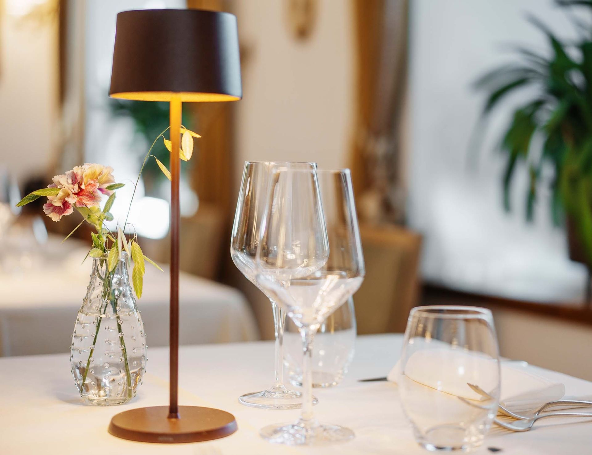 Ein Tisch mit einer Lampe, Weingläsern und einer Vase mit Blumen darauf.