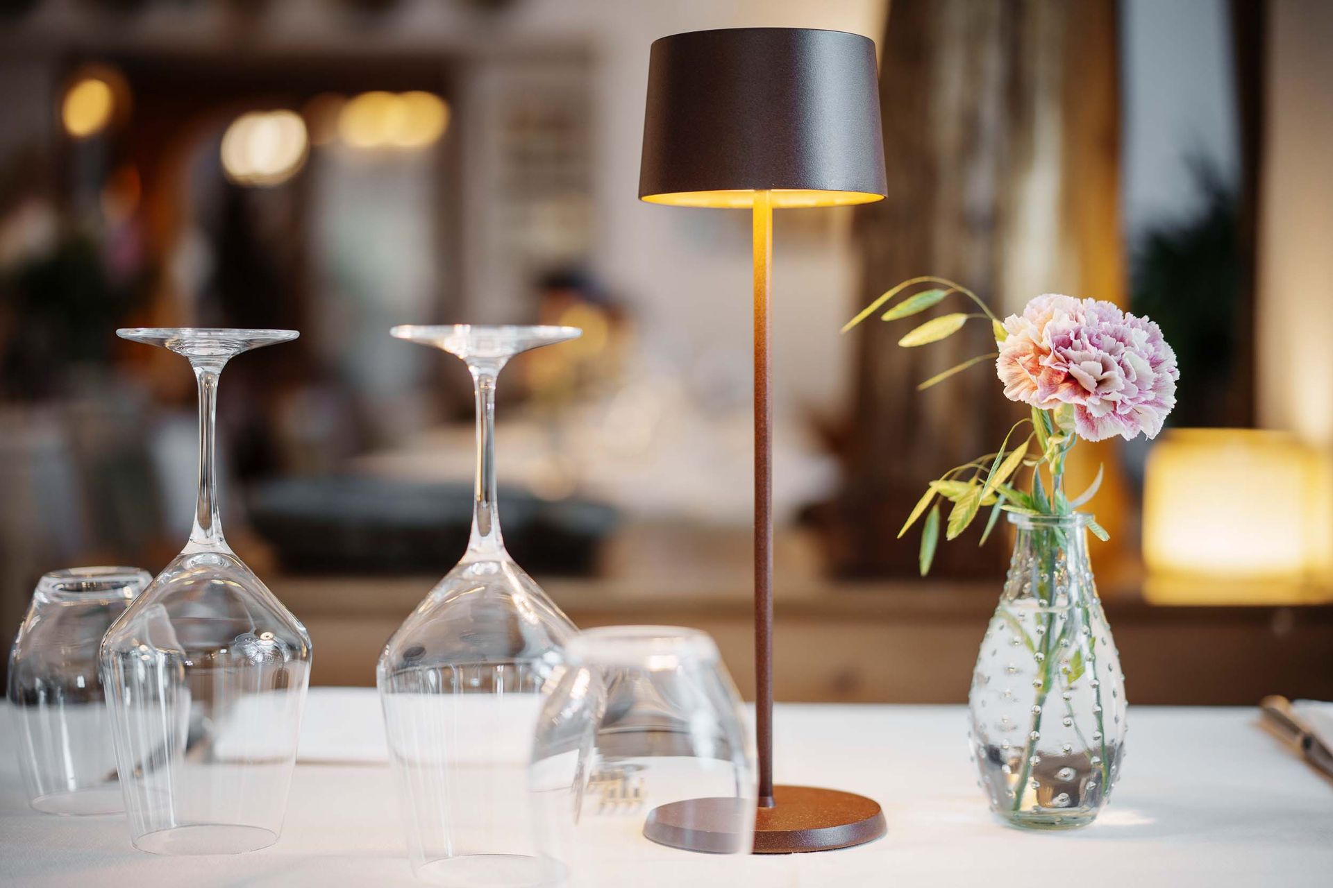 Ein Tisch mit Weingläsern, einer Lampe und einer Vase mit Blumen.