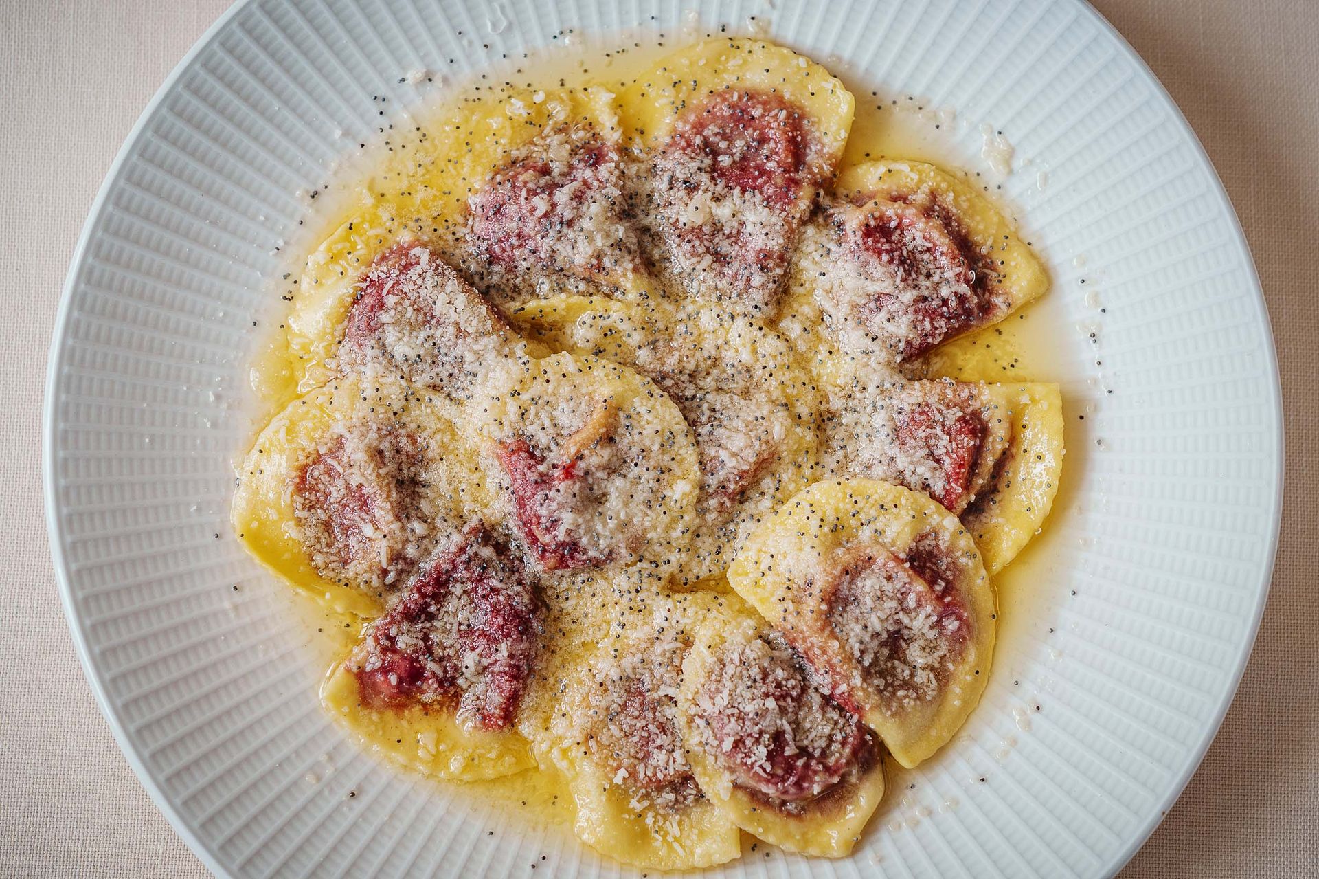 Ein weißer Teller mit Ravioli und Fleisch auf einem Tisch.