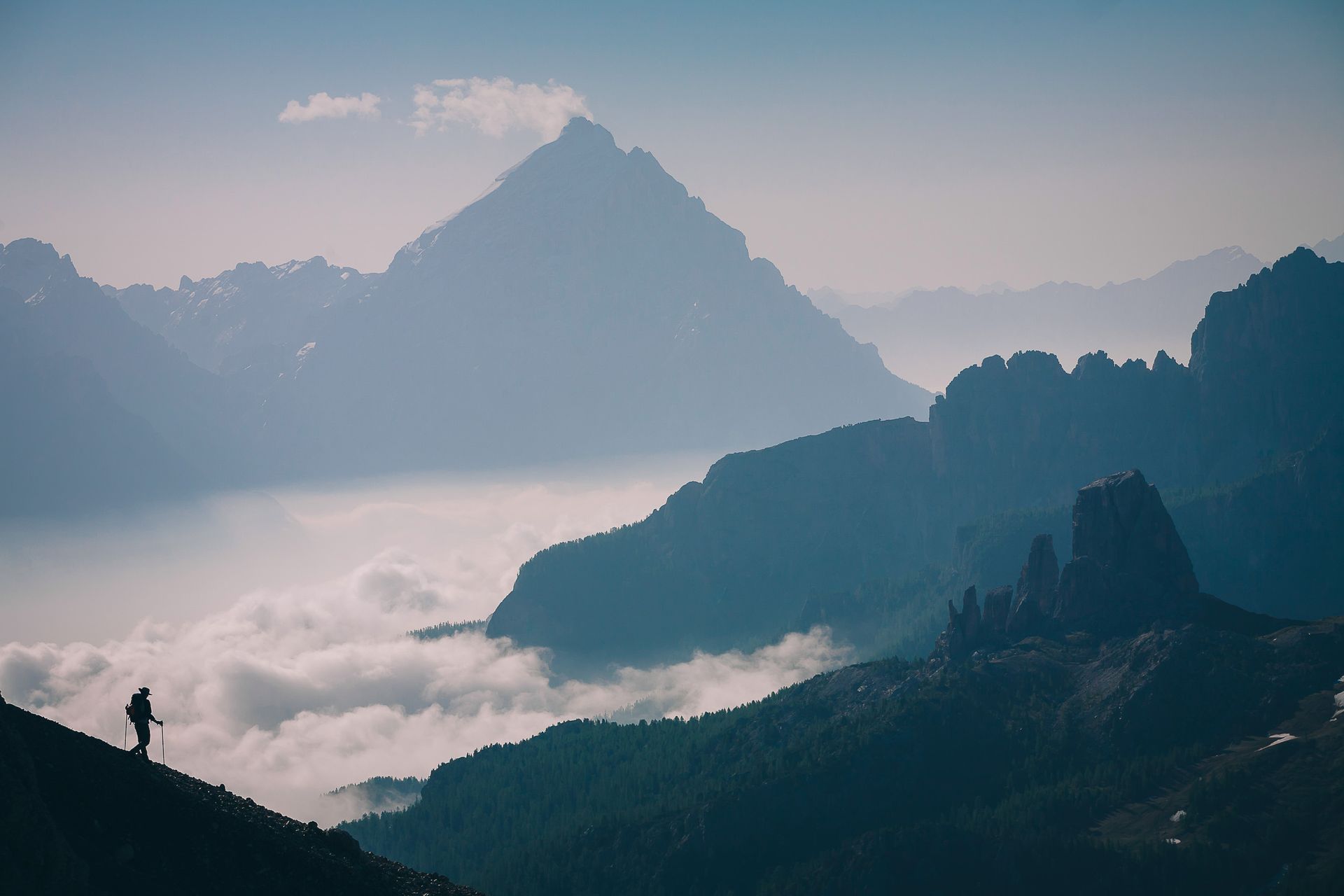 Eine Person steht auf einem Berggipfel, umgeben von Wolken.