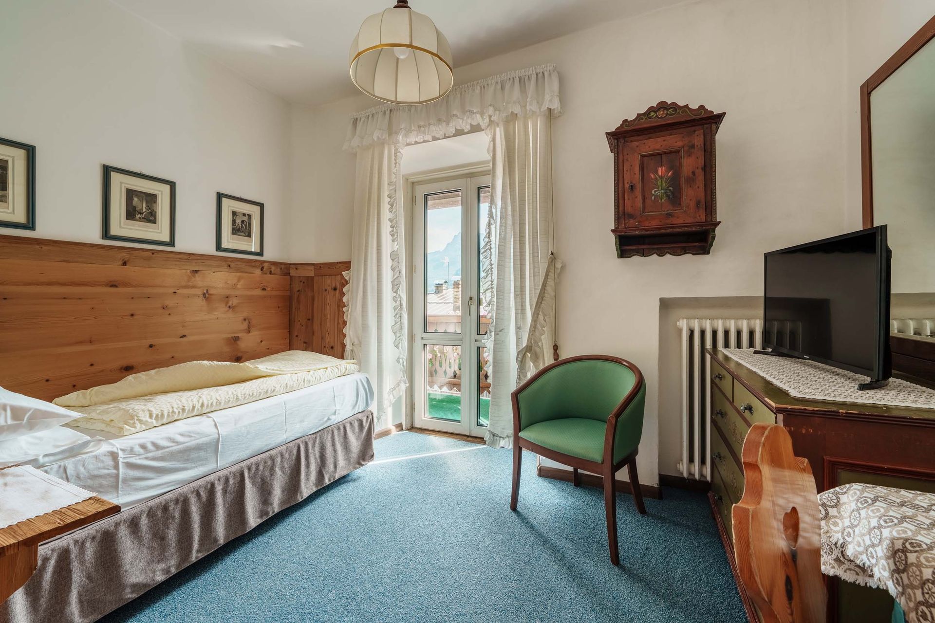 Ein Hotelzimmer mit Einzelbett, Sessel, Fernseher und Spiegel.