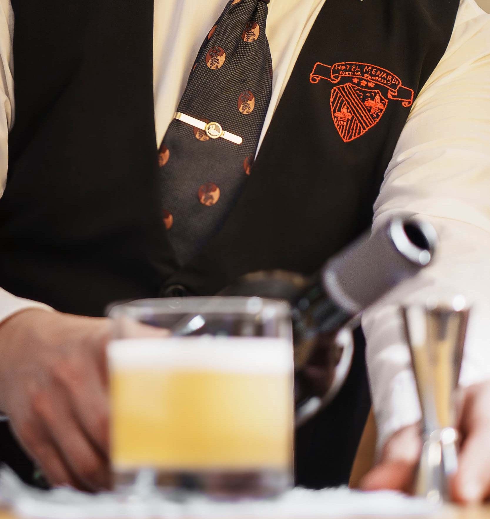 Ein Mann in einer schwarzen Weste und Krawatte gießt ein Getränk in ein Glas
