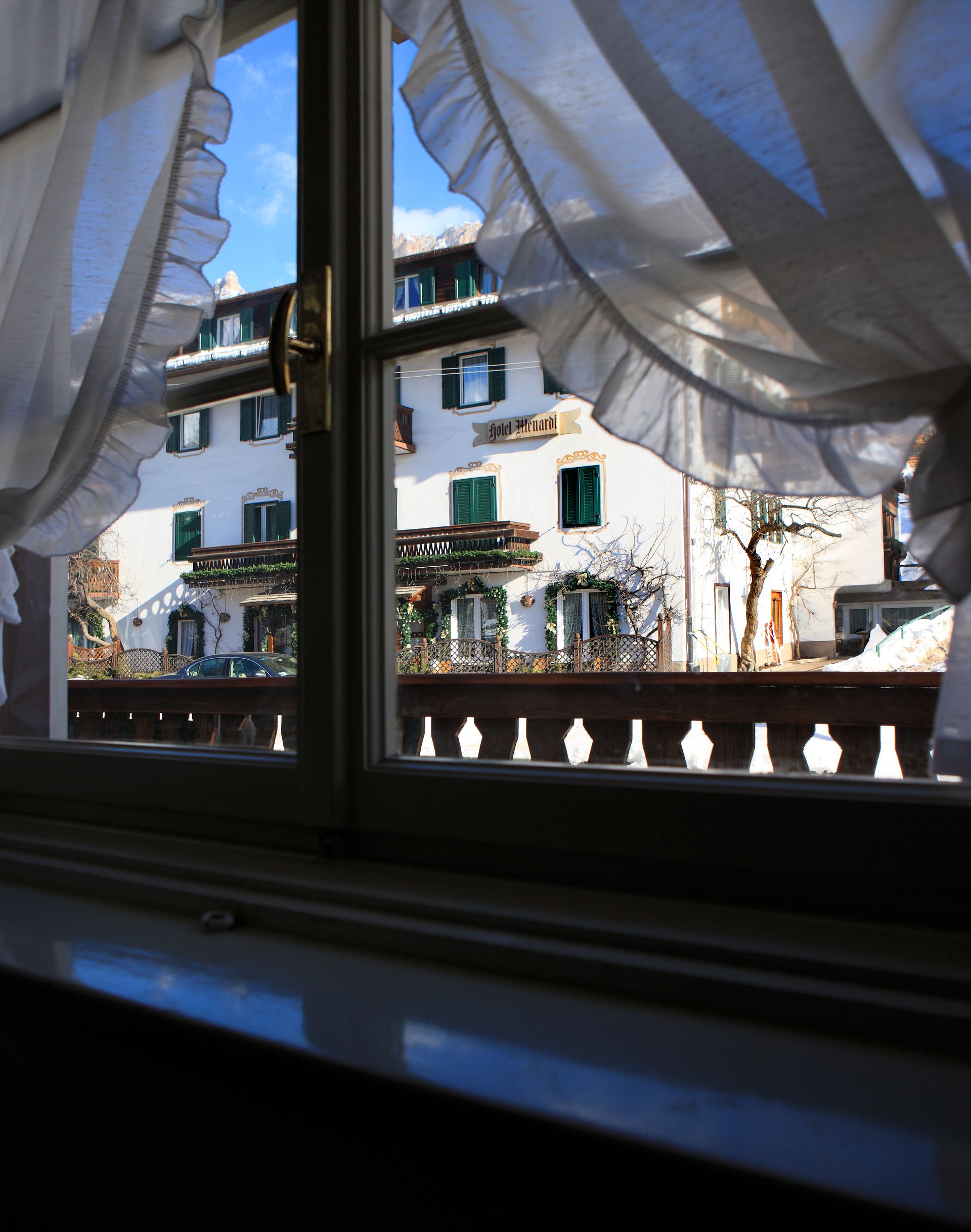 Blick auf Hotel Menardi durch ein Fenster mit gerüschten Vorhängen