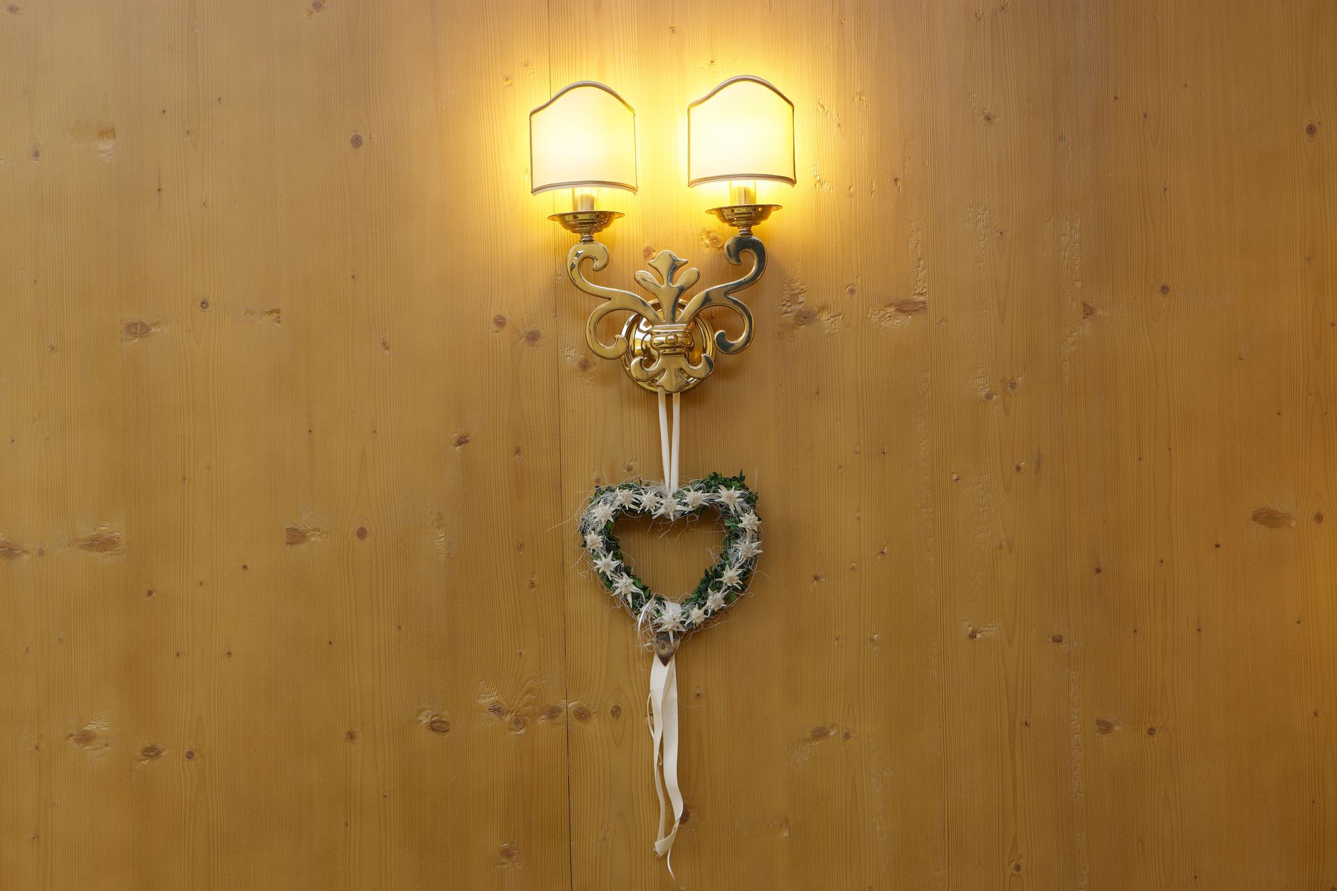 Ein herzförmiger Kranz hängt an einer Holzwand neben einer Lampe.