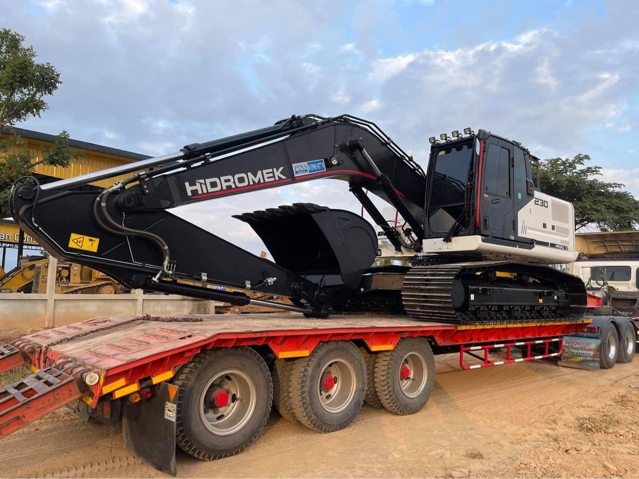 Large black excavator loaded on a red flatbed trailer in an outdoor dirt lot