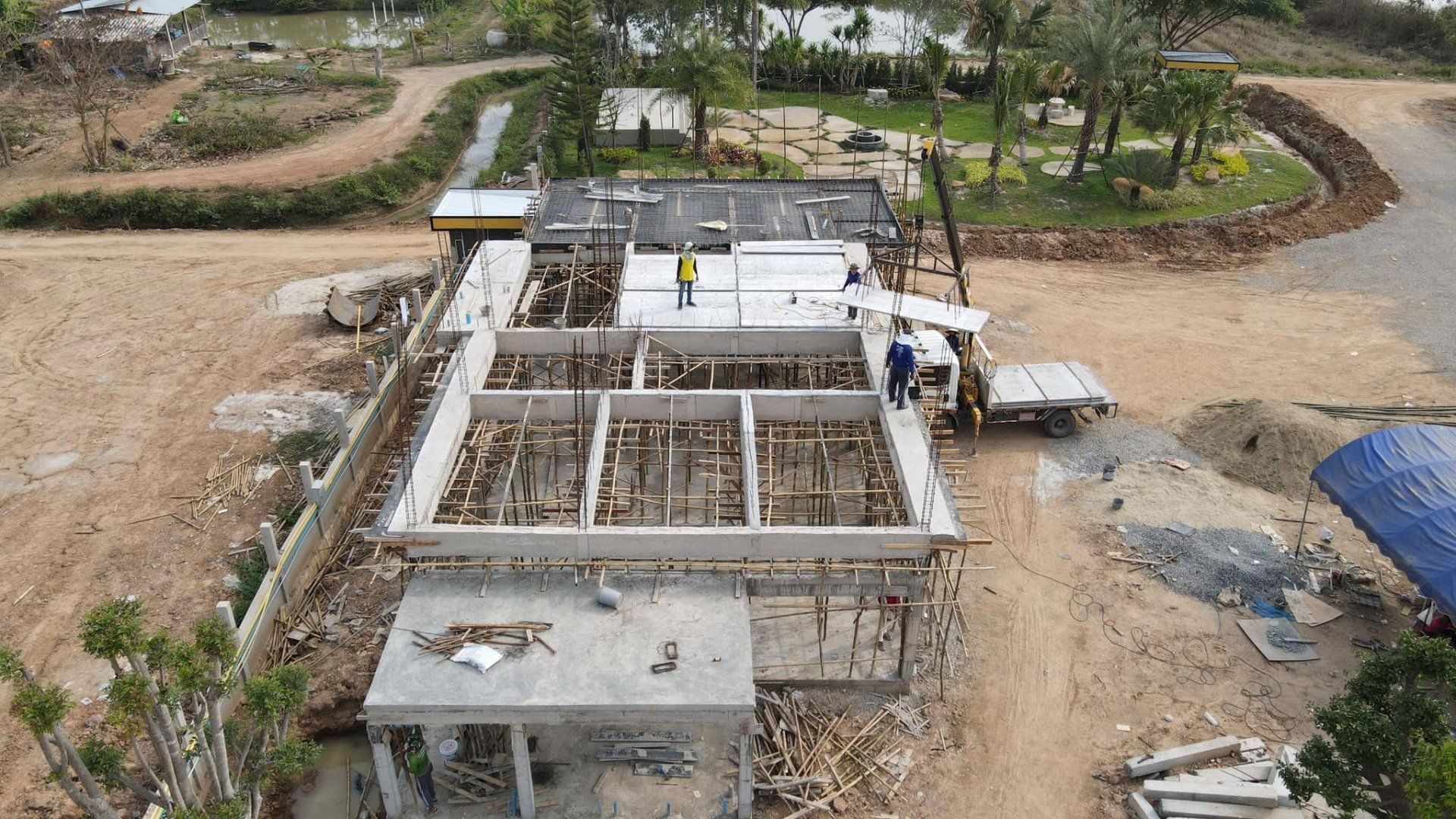 Aerial view of a concrete building under construction beside dirt roads and trees.