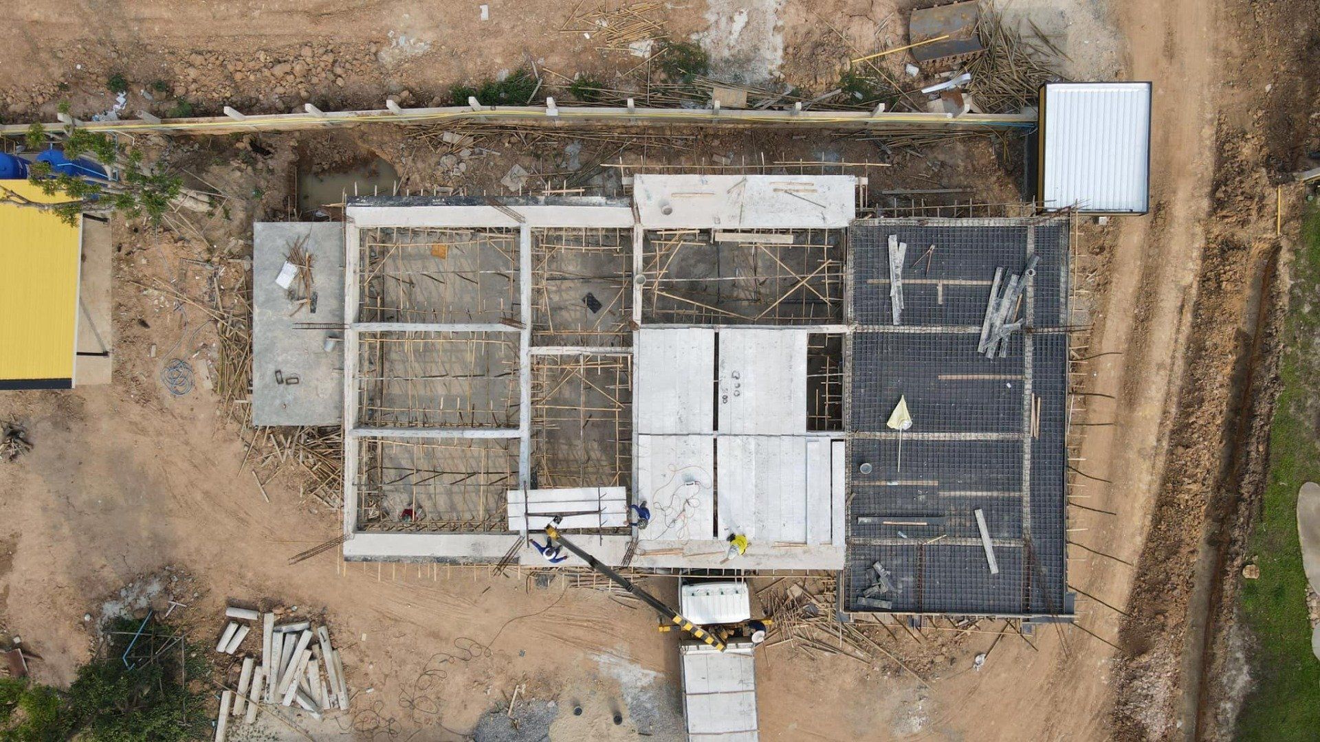 Aerial view of a construction site with concrete foundations, white panels, and dirt roads around it