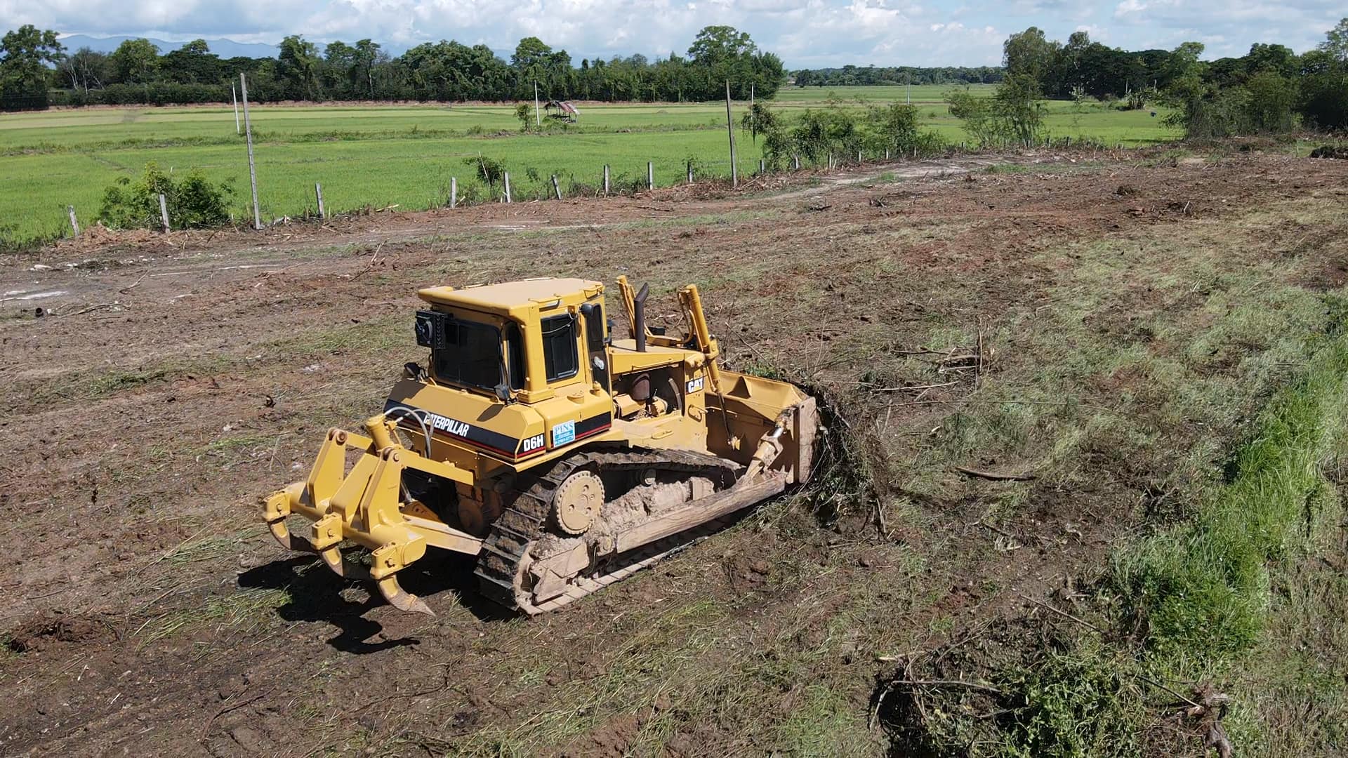 Yellow bulldozer grading a dirt field in a rural landscape