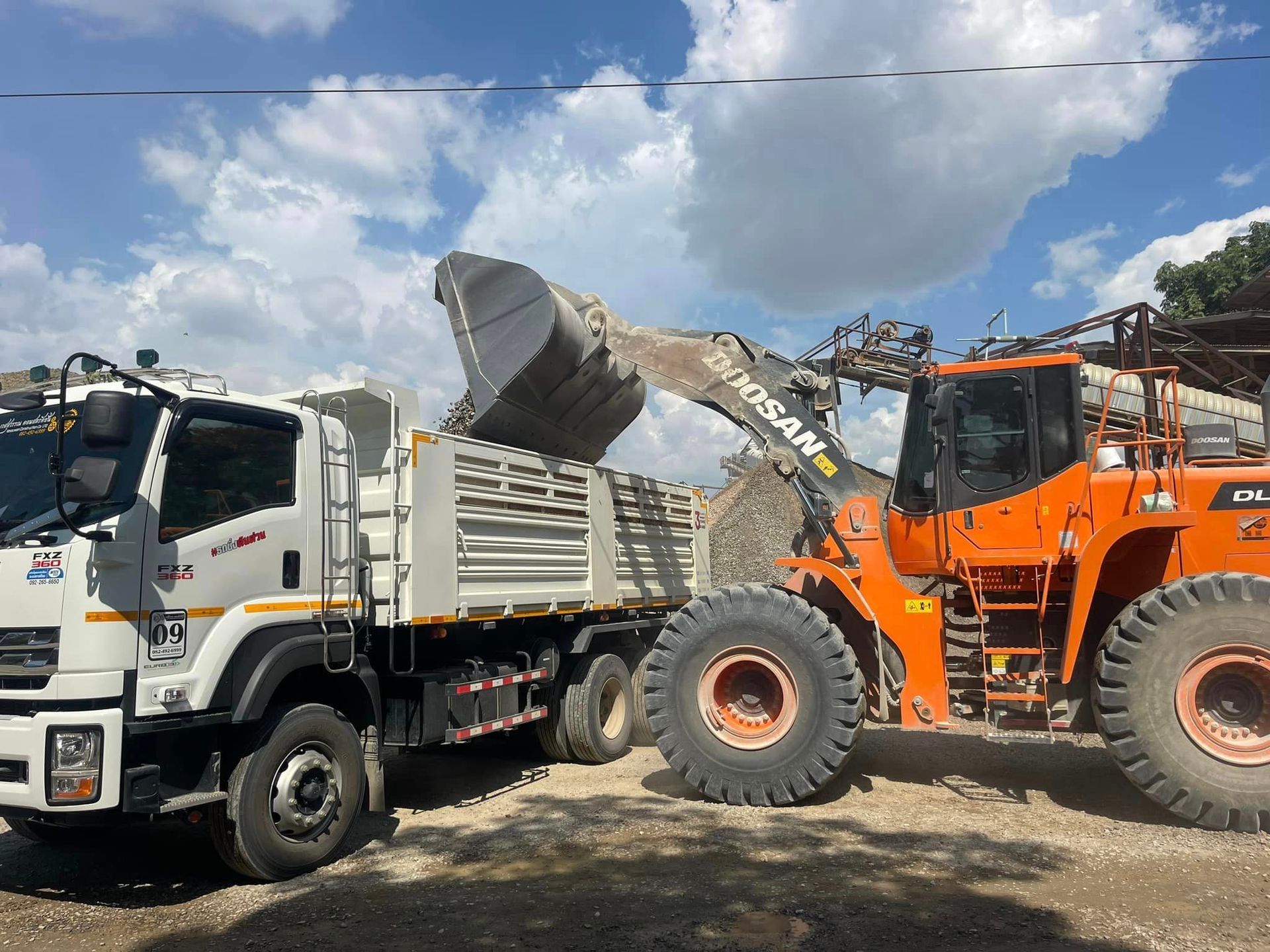 Orange front loader tipping gravel into a white dump truck under a cloudy sky