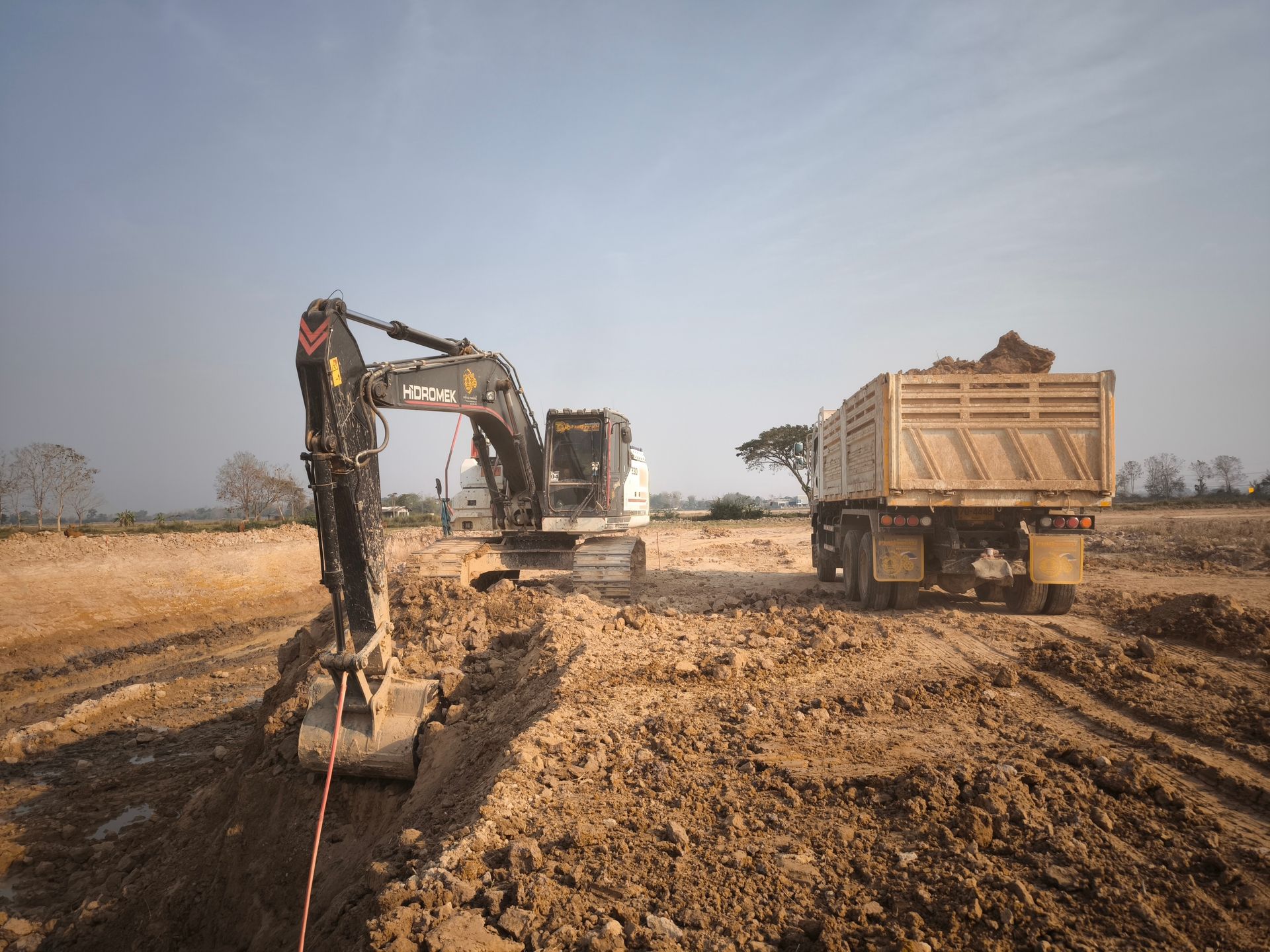 Excavator and dump truck at a muddy construction site under a clear sky